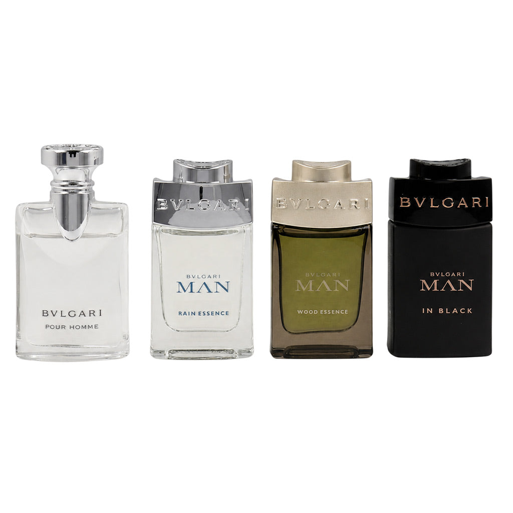 Four Bvlgari Man fragrance bottles arranged in a row on a white background: Pour Homme in clear glass with silver cap, Rain Essence in clear glass with silver cap and blue lettering, Wood Essence in olive-green glass with gold cap, and In Black in black glass with gold lettering.