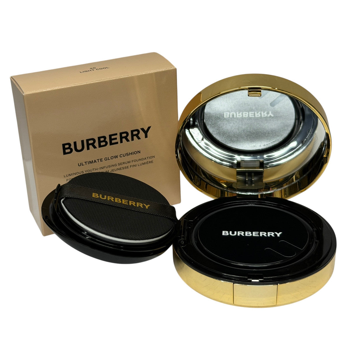 Burberry Ultimate Glow Cushion compact shown open with the gold-toned cushion base, black lid, and branded box on a white background.