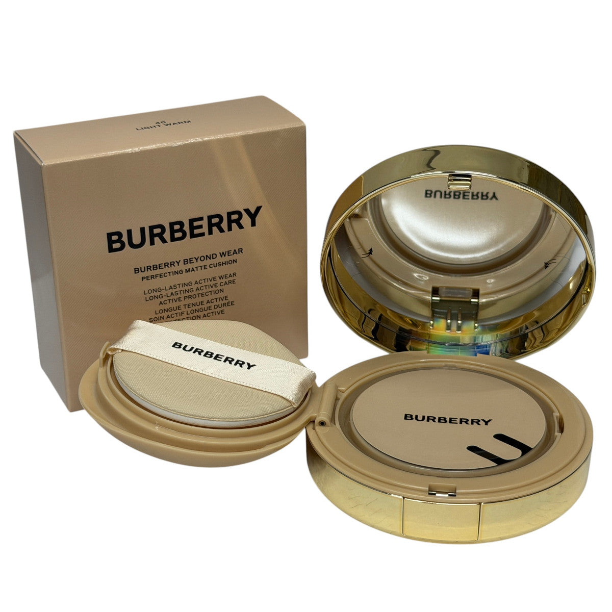 Burberry Beyond Wear long-lasting matte cushion foundation shown with its gold box, open gold compact, and applicator puff on a white background.