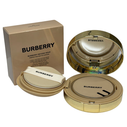 Burberry Beyond Wear long-lasting matte cushion foundation shown with its gold box, open gold compact, and applicator puff on a white background.