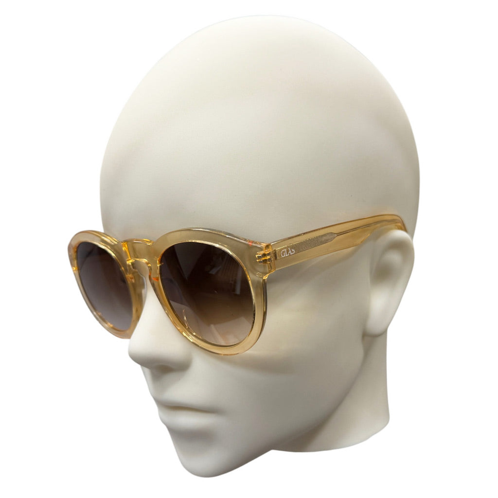 Oversized round sunglasses with a translucent gold acetate frame and dark brown gradient lenses, displayed on a white mannequin head against a white background.