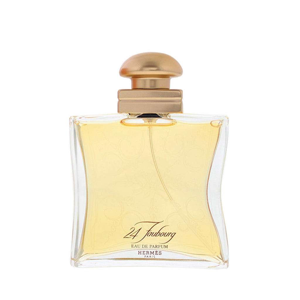 Hermes 24 Foubourg Eau de Parfum bottle with a curved clear glass body, pale yellow liquid, and a metallic gold cap, shown on a white background.