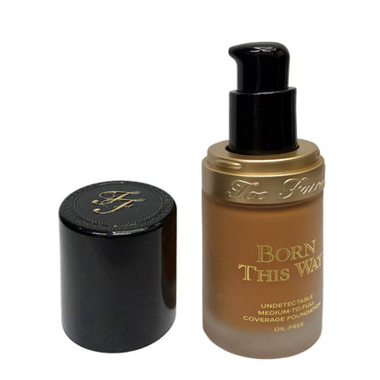 Too Faced 'Born This Way' liquid foundation in a clear bottle showing the medium brown shade, with its black pump dispenser and separate black cap displayed next to it on a white background.