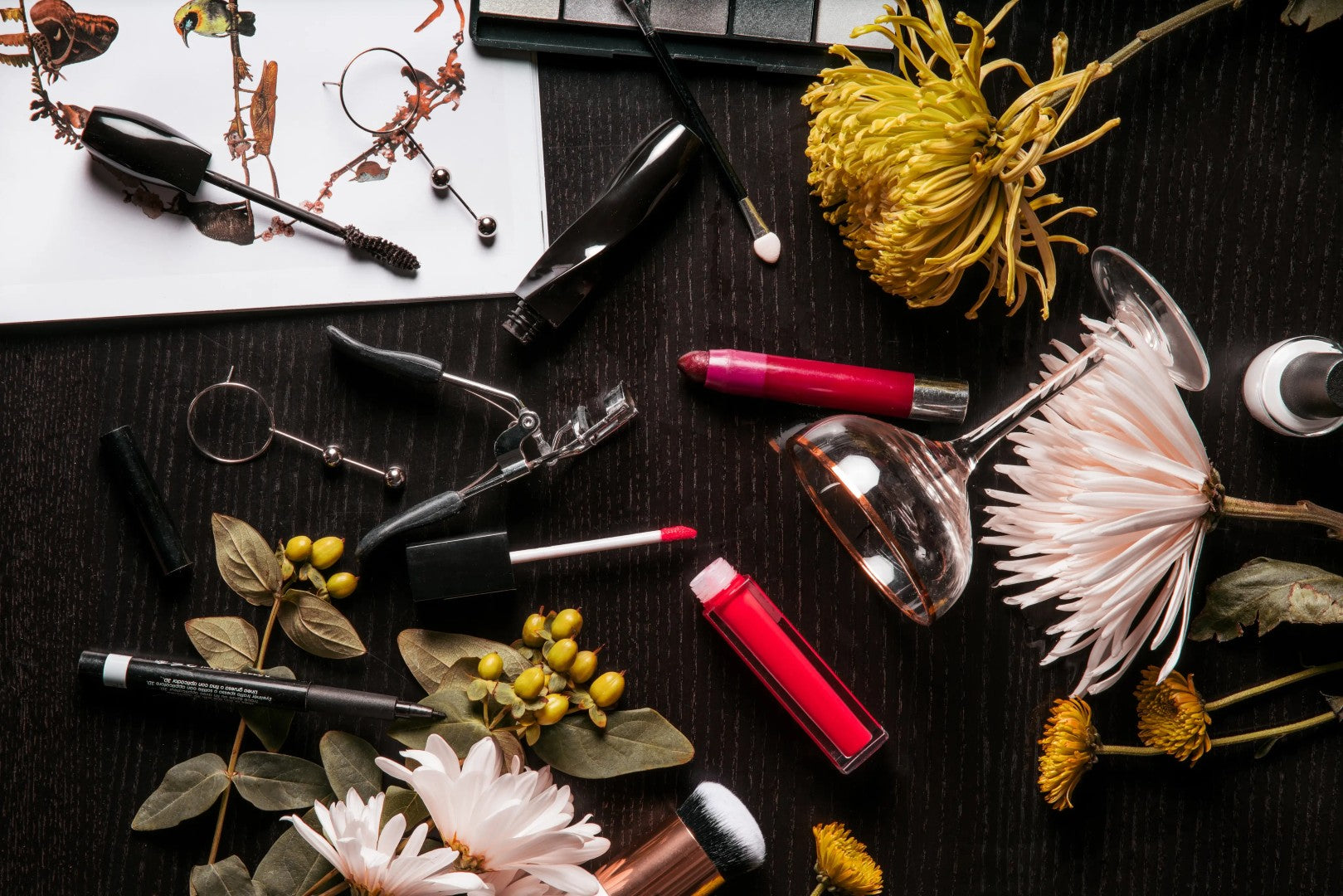 Makeup items including lipsticks, brushes, and flowers on a dark surface