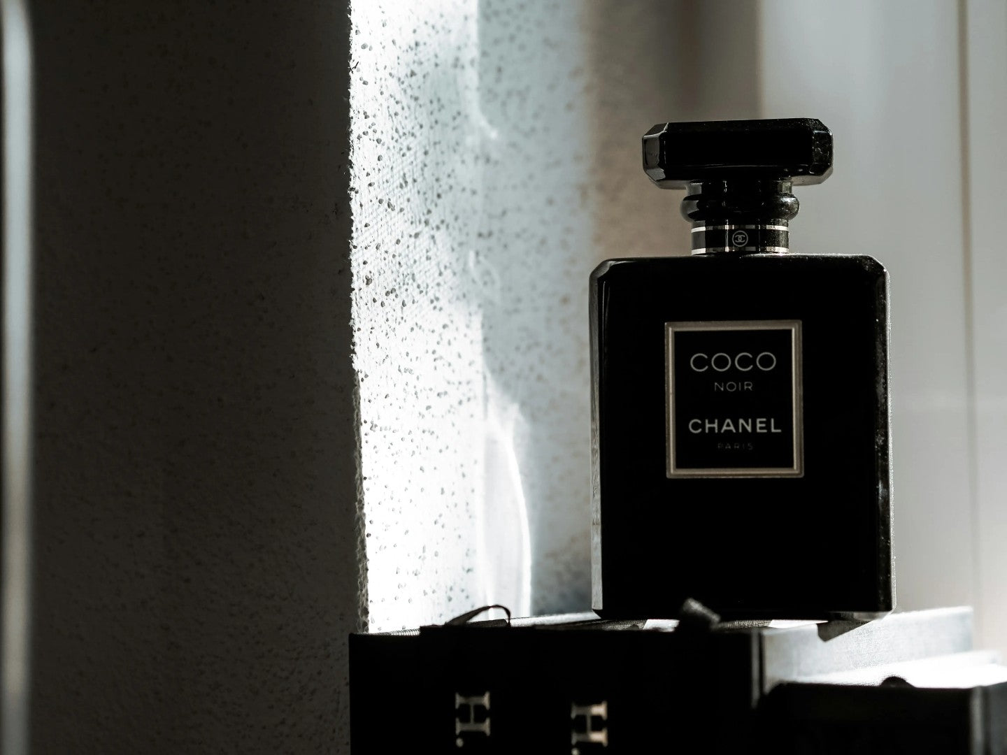 Black Chanel Coco Noir perfume bottle on a textured surface with light casting shadows.