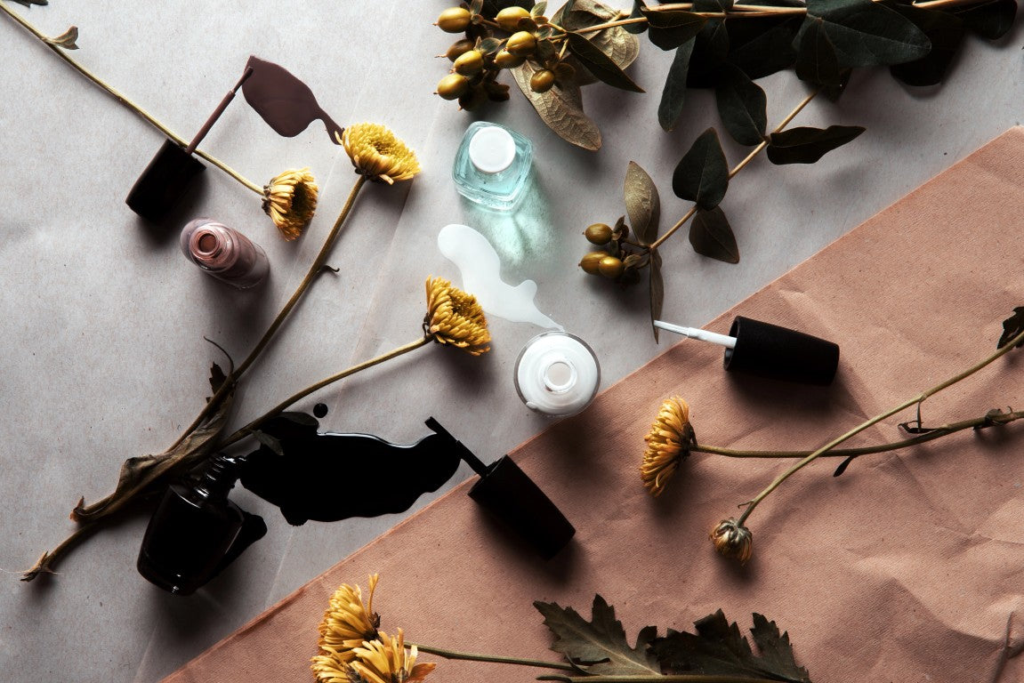 Cosmetic bottles with black and white caps on a gray surface with dried flowers and leaves.
